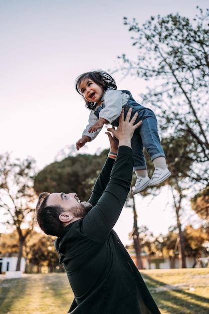 Father has fun with his daughter in the park throwing her in the air while she laughs happily