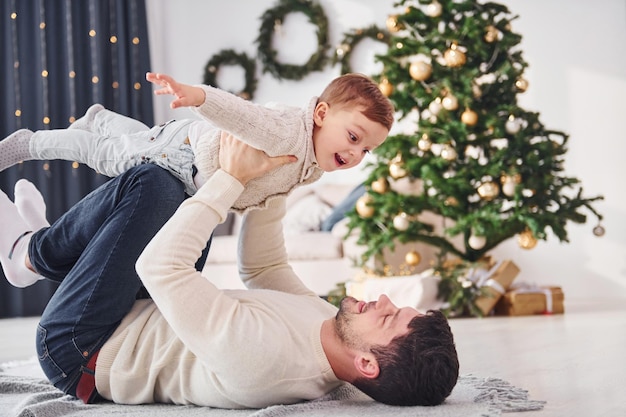 Father having fun with his son indoors in the christmas decorated domestic room