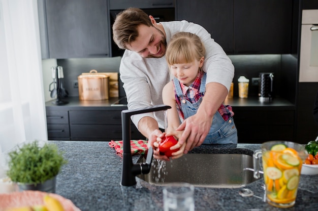 Photo father helping girl to wash pepper