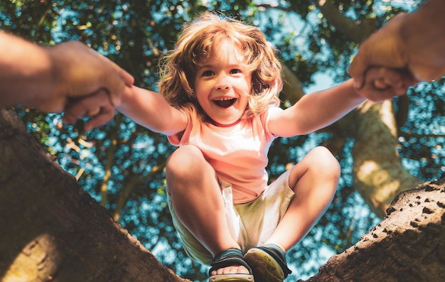 父は息子が木に登るのを手伝っています夏の間に木に登る幸せな男の子父親は子供protを手渡します