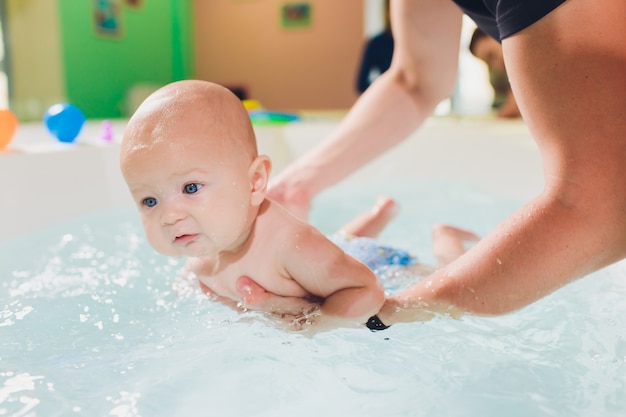 A father helps is infant boy during swimming lessons in the pool.