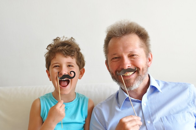 Photo father and his cute little son put on paper beard and smile happy fathers day