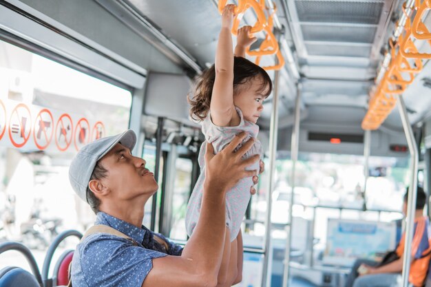 Father and his daughter playing while riding public transport hanging on handle bar