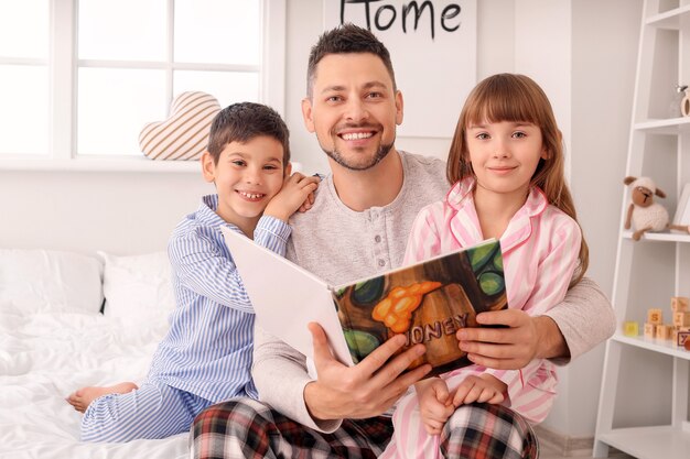 Отец и его маленькие дети читают сказку на ночь дома
