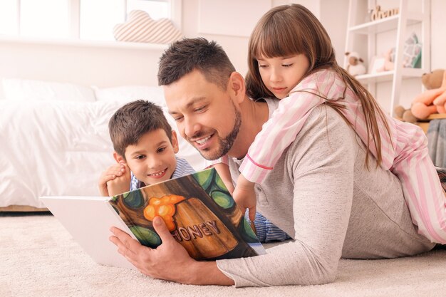 Padre e figli piccoli che leggono la favola della buonanotte a casa