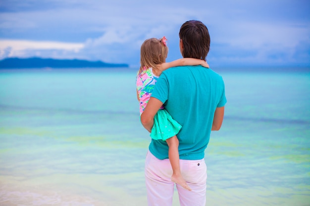 Father and his little daughter looking on the sea at tropical beach