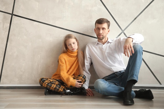 Father and his little daughter sitting together against the wall