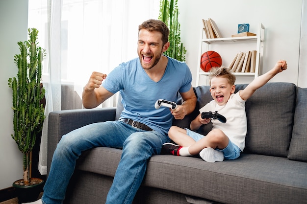 Father and his little son playing video games together on couch at home