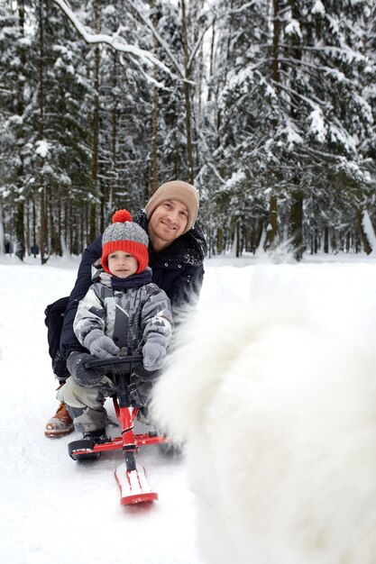 Photo father and his son in funny hat having fun and laughing in snowy winter forest happy family wearing warm winter clothes enjoying wintertime in snow covered pine forest outdoor activities with kids