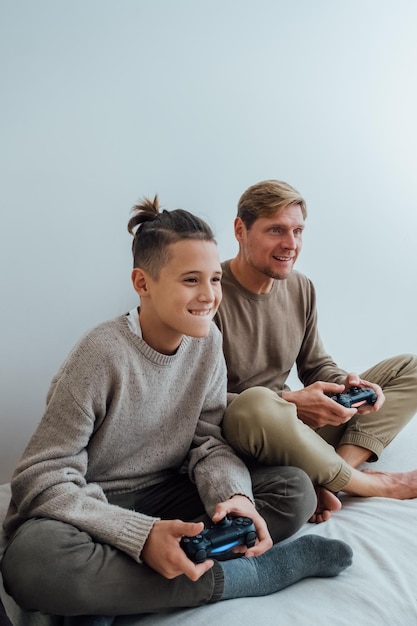 Photo father and his teenager son with joysticks playing video games at home