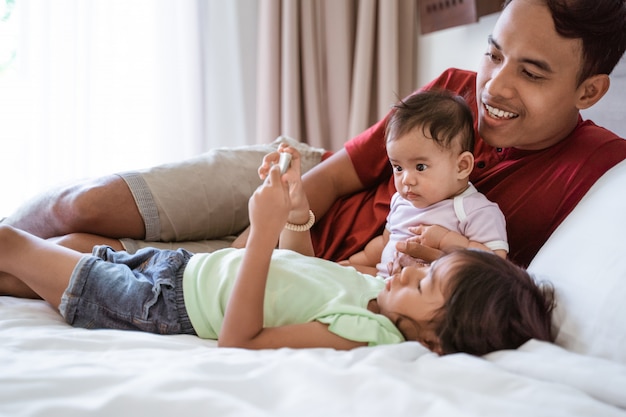 Father and his two daughters lay in bed while looking at a video