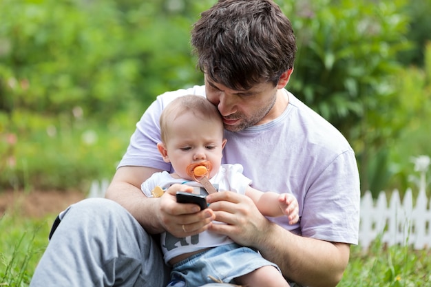 Father holding a baby and texting on his mobile