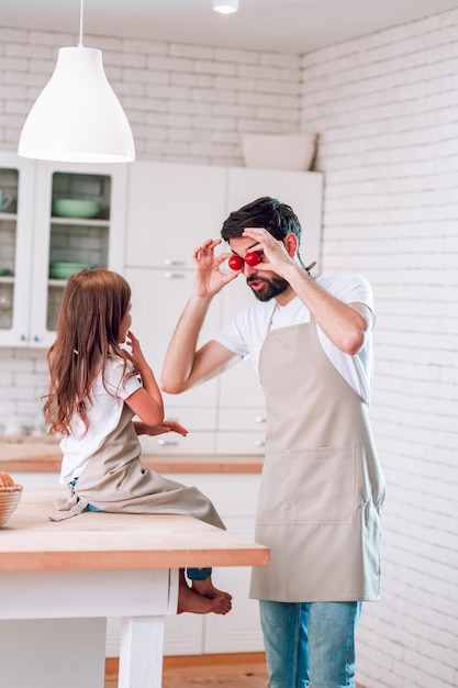 Father holding cherry tomatoes on his eyes with small girl near on the kitchen