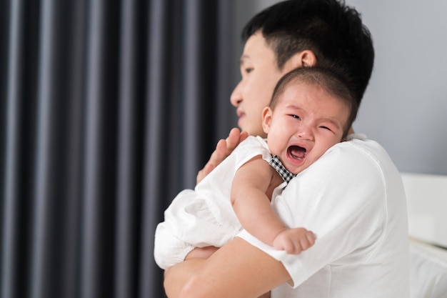 Father holding crying baby on a bed