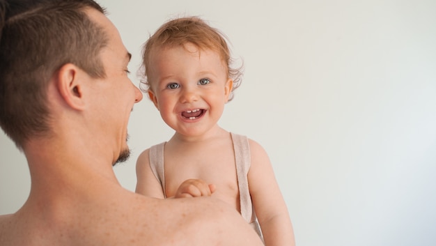 Father holding a cute little smiling baby in his arms on a white background