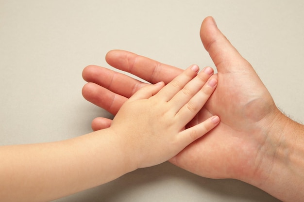 Father holding daughter hand on grey background