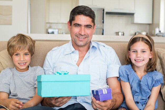 Father holding gifts by children on sofa