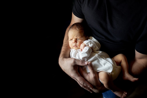 Father holding his 15 days old son in his hand on black background.