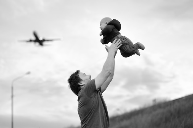 Father holding his baby and airplane on the sky