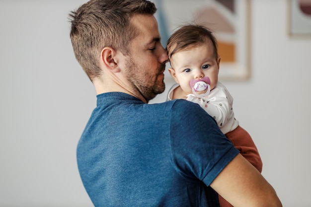 Photo father holding little daughter with pacifier in the arms