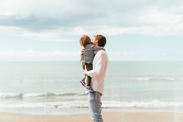 Photo father holding toddler son on seashore