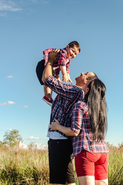 A father holding up his son, while the mother hugs him, in the meadow