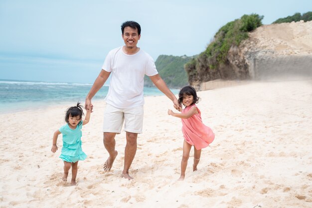 Отец держит в руках две дочери на пляже