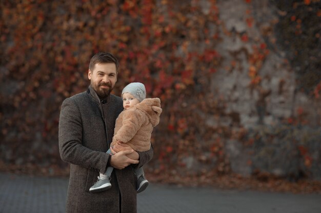 Father holds his daughter in his arms during a walk in the park in the fall.