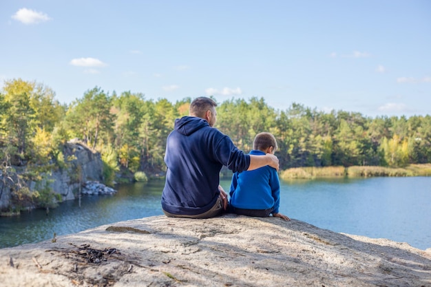 Padre abbraccio suo figlio godendo del tempo trascorso insieme tra padre e figlio bambino felice sorridente a trentadue denti bosco autunnale genitore figlio famiglia felice all'aperto