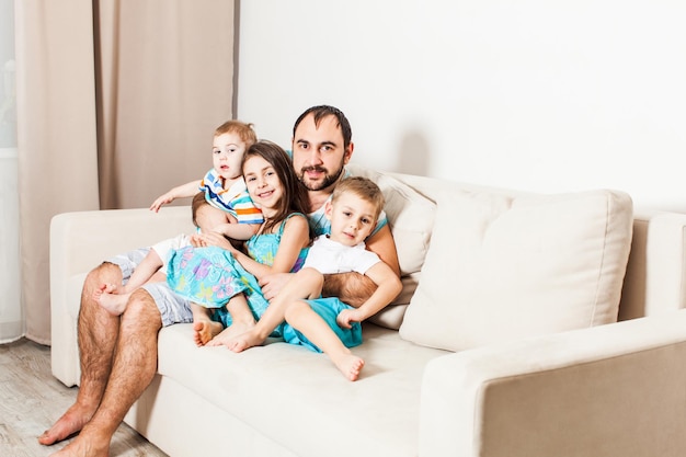 Father hugs his three kids. Portrait of young man with children sitting on the couch.