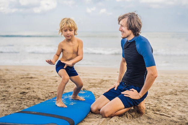 Father or instructor teaching his 4 year old son how to surf in the sea on vacation or holiday Travel and sports with children concept Surfing lesson for kids