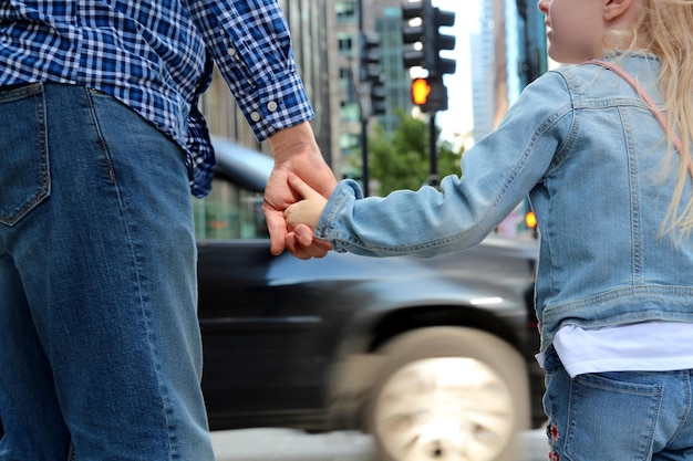 Photo father is holding the daughters hand on a crosswalk traffic lights ahead