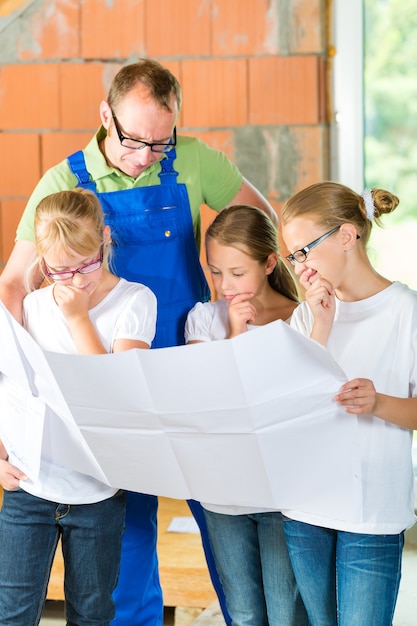 Padre e figli o figlie e amici che esaminano un piano di costruzione in un cantiere