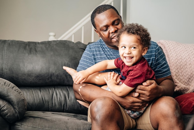 Foto padre e figli a casa a giocare sul divano afroamericano o padre nero con i suoi figli