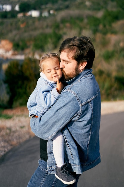father kissing daughter while standing on road