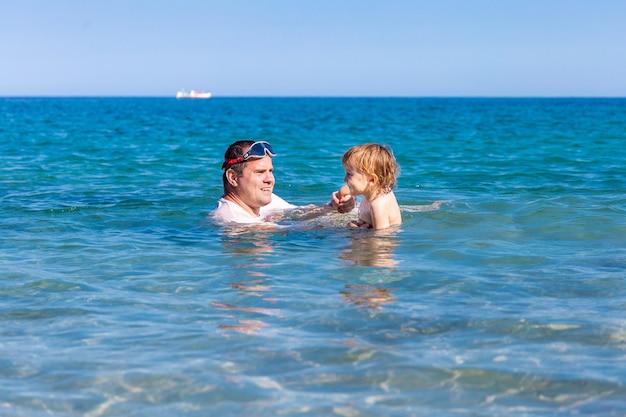 Father and little son having fun swimming and playing together in sea water at summer holidays