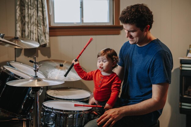 Photo father looking at cute baby son making face while playing drums