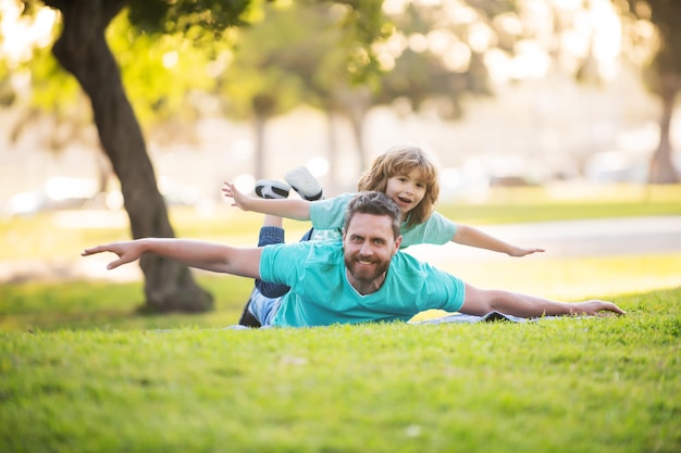 Padre sdraiato sull'erba con bambino felice eccitato figlio sulla spalla famiglia di due generazioni di uomini spensierata che si divertono concetto di famiglia uomo del fine settimana