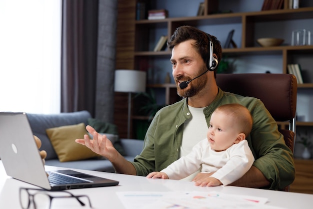 Father on maternity leave holding an online conference a meeting in the home office with a small child in his arms Dad with a child Freelancer combines child care and work Paternity leave