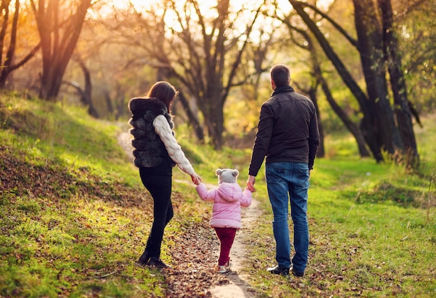 Father, mother and baby walking on autumn colorful leaves and grass background. Bright back light.