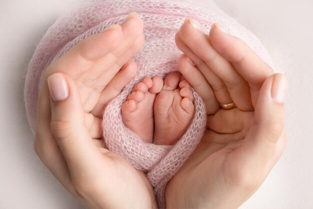 A father and mother hold the feet of a newborn child in a pink blanket on a white background barefoot