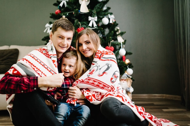 The father, mother holds little son sitting near Christmas tree. Happy New Year and Merry Christmas. Christmas decorated interior. The concept of family holiday. Portrait. upper half. Close up.