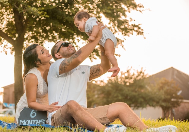 father and mother playing with cute son while sitting on grassy field