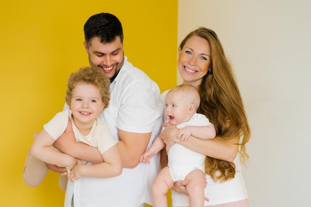 Father and mother stand side by side on a yellow background and hold the brothers' children in their arms a man and a woman are happy with their family