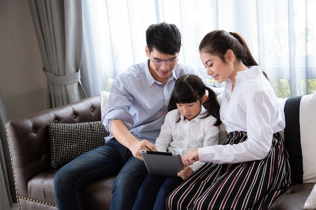 父と母子供たちにタブレットを使って家で宿題をすることを教えるアジアの家族は幸せです