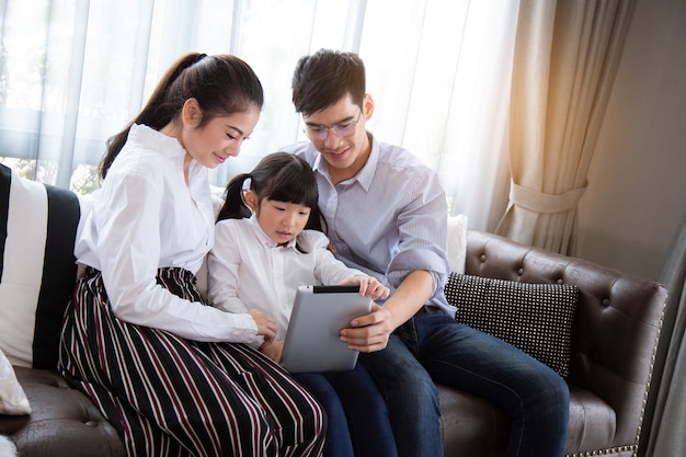 父と母子供たちにタブレットを使って家で宿題をすることを教えるアジアの家族は幸せです