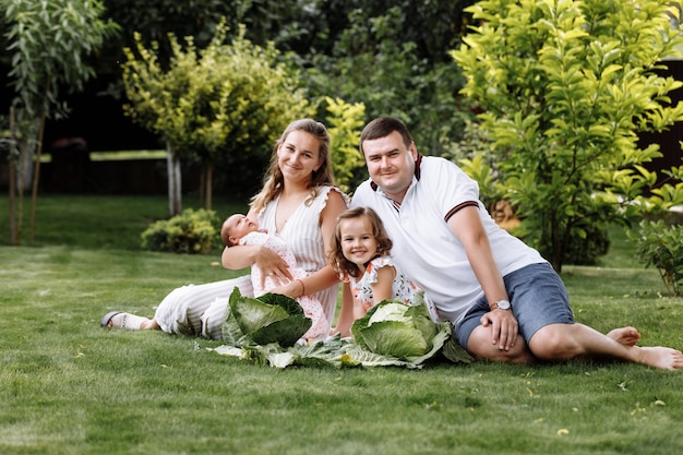 Father, mother and two children, baby girl and little daughter on the grass with cabbages