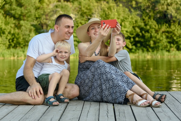 Photo father mother and two little sons are sitting and taking selfies