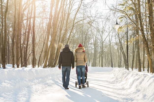 Father and mother with baby carriage in winter forest.