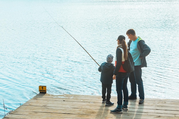 Father and mother with boy kid playing with bench near water